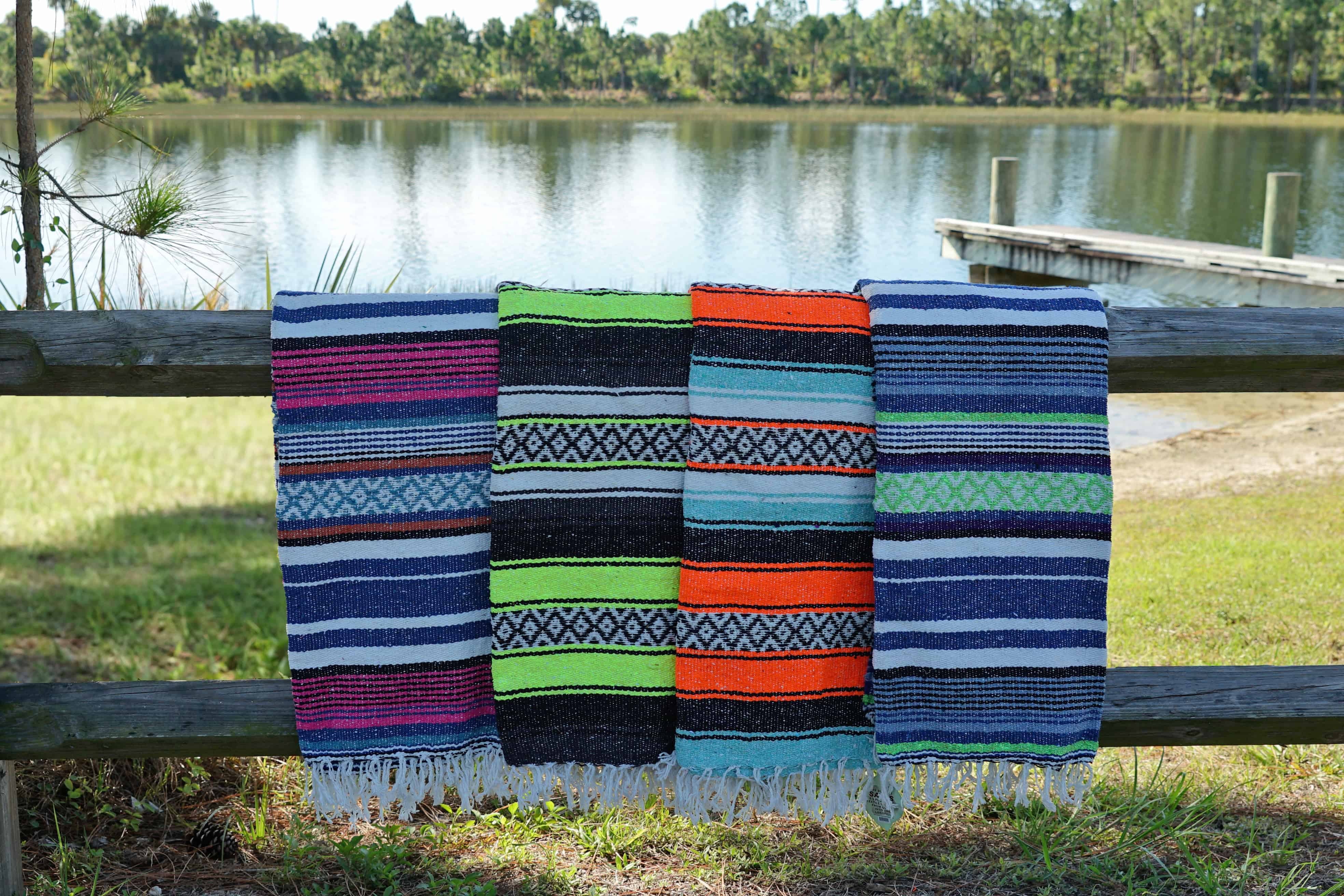 Earth Ragz Mexican blankets in bright colors displayed on a wooden fence beside a lake