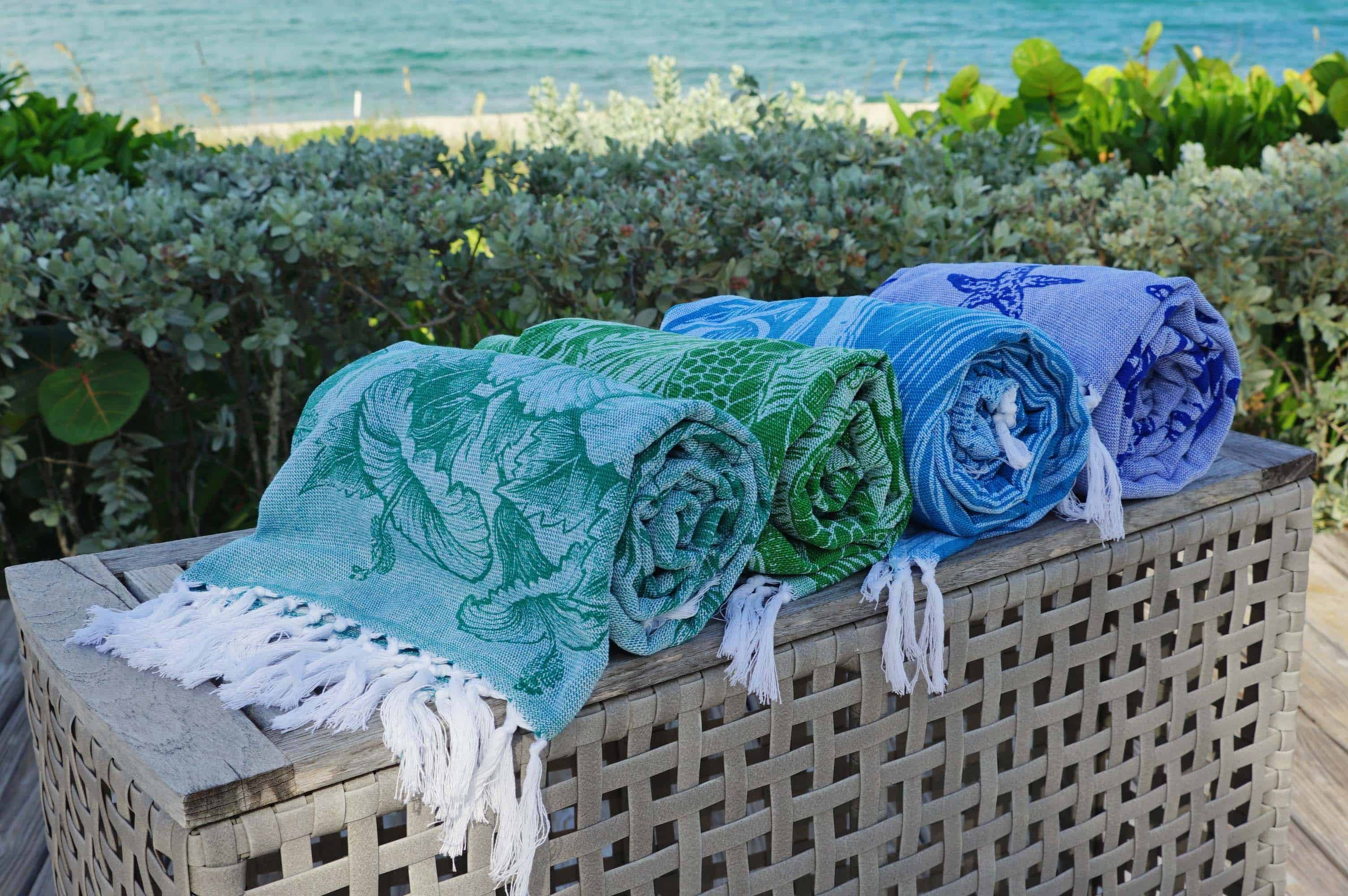 Rolled Earth Ragz sand-free towels in coastal colors displayed outdoors near the beach