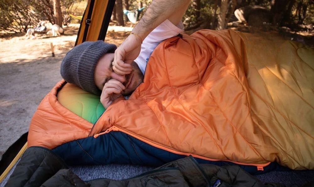 Person waking up in a technical puffy blanket inside a car camping setup